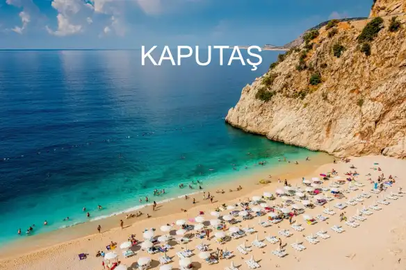 Bir plaj düşünün tam kanyon ağzında olsun, bembeyaz kumları ve turkuaz sularıyla sizi karşılasın, tepesinden fotoğraf çekmeye doyamayacağınız manzarasıyla da sizi büyülesin. Kaputaş Plajı tabiri caizse tam da böyle yer. Kaş ile Kalkan arasındaki sahil yolu üzerinde, Kalkan’a 2 km uzaklıkta bulunan bu benzersiz plajın suyu, yer altından akan suların deniz kenarında kumlar arasından süzülmesi sonucu serin ve turkuaz renktedir. Plaj herkese açık ancak ona ulaşmak için tam 187 basamak inmeniz gerekiyor. Yani tepelerin altındaki bu turkuaz cennete ulaşmanız için biraz emek harcamak gerekiyor deyim yerindeyse. Kaputaş plajı, her yaz yerli yabancı pek çok ziyaretçi ağırlıyor. Bu anlamda Antalya turizmine katkısı yadsınamaz bir gerçek. Ancak plajın öyle bir özelliği var ki; hani uzun bir kara yolculuğu sonunda yazın kavurucu sıcağı sizi bunaltmış kendinizi serin sulara bırakmak istersiniz, bir de hiç beklemediğiniz bir anda çölde karşınıza göz alıcı bir vaha çıkar ya tam da böyle bir yer işte. Eğer bir tekneniz varsa, plajın sakin koyunda da Kaputaş’ın tadını çıkarabilirsiniz elbette. Plaj, Ege’nin çoğu plajı uzun göz alıcı bir uzunlukta değil belki ama etrafını çevreleyen yüksek kayalıklarla diğer plajlardan ciddi bir şekilde ayrılıyor. Kaputaş Plajı, Antalya’ya il sınırları içinde bulunsa da, civardaki birçok merkeze de oldukça yakın. Hava yolu ile yolculuk yapacaksanız özellikle Dalaman havaalanını tercih etmelisiniz zira Antalya’ya nazaran Dalaman’a daha yakın bir konumda. Ulaşımı her açıdan kolay bir noktada olan Kaputaş plajının tek sıkıntısı otopark alanının yok denecek kadar kısıtlı olması. Bu sorunu çözdükten sonra ise, her şeyi unutup doğa harikası plajın tadını, gün rengini kızıla döndürene kadar yaşayacaksınız. Yüzmek ayrı bir keyif hele de dalışa meraklı olan deniz tutkunları için ise vazgeçilmez bir hobi. Ancak çoğu insan yüzme deneyimini de göz alıcı mavilikte, baş döndüren dinginlikte ve özellikle yaz sıcaklarını unutturacak sularda yüzmek ister öyle değil mi? “Kızgın kumlardan serin sulara” denilen gerçeği tam anlamıyla yaşama garantisi sunuyor siz tatilcilere Kaputaş Plajı. Tabi bu deneyime kavuşmak için küçük bir bedel ödemeniz gerekiyor. Zira şemsiye ve şezlong kiralamak ücrete tabi. Ancak kendi şemsiyenizi de yanınızda getirebilirsiniz. İlla ki plajın şemsiyesini kullanmak zorunluluğunuz yok elbette. Eklemek istediğimiz diğer bir noktada ne yiyeceksiniz? Kaputaş plajını gidecekseniz yanınızda yiyecek içecek bir şeyler götürmeniz gerekmektedir. Çünkü bu doğal alan koruma altında olduğu için etrafında yapılaşmaya izin verilmediği gibi büfe, kafe yerler de bulmanız imkansız. İster havadan ister karadan şahane bir manzara sunan bu engin turkuaz sularla gördüklerinizle yetinmeyin, tatil planınızı yaparken görülecekler listenize Kaputaş Plajını eklemeyi unutmayın. Bizden söylemesi.