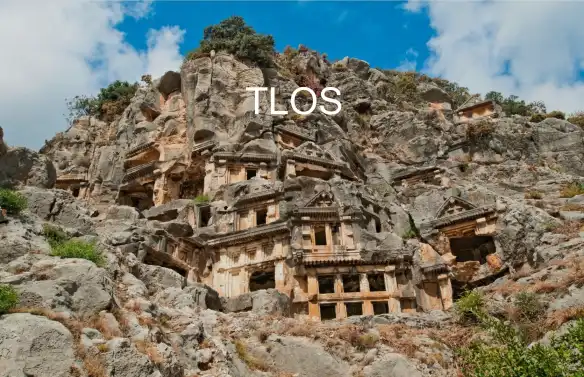 Tlos Antik Kenti’n dağlık bir arazide konumlanmış olması dönemde ne derece çetin savaşlar ve savunma geçirdiğini kanıtlar nitelikte. Zamanında Likyalıların yoğun hüküm sürdüğü bölgenin en eski yerleşim yeri Tlos. Dönemin en göze çarpan eserlerinden olan kayalara oyulmuş mezarlar mimari ve dini açıdan da bölgenin zenginliğini yansıtan en önemli kalıntılar. Bunca mezar içinde en görkemli, ihtişamlı ve dikkat çekici olan ise Pegasus’a ait mezar. Özellikle de, Pegasus’un, üç başlı canavar olduğuna inanılan Chimera ile savaşının resmedildiği Bellerephontes’e ait mezar anıtı en dikkat çekici yapılardandır. Mezar odasına süslemeli iki kapıdan girilir. Ziyaretiniz esnasında büyülenmemeniz neredeyse imkansız. Bazı kültür ve tarihsel turizmi seven tatilcilerin defterleri bu antik eserlerle çizili. Bölgeye gezi yapacaksanız siz de karalama defterinizi hazırlayın. Gördüğünüz her kalıntıyı defterinize karalayıp onları resmetmek isteyeceksiniz. Tlos için tertemiz bir sayfa ayırın, ihtişamı karalama defterinizi de fazlasıyla kaplayacak. Tlos Antik Kenti içinde, tanrıların tanrısı olduğuna inanılan Kronos’un da tapınağı mevcut. Biraz deformasyon dışında günümüzde varlığını gösteren sadece tiyatro, stadyum, büyük ve küçük hamam, Nekropol kalmıştır. Ancak bu yapılar bile, Tlos’un dönemin ötesinde gelişmişlik ve kültürel yapısını göstermek için yeterli. Tarihi yapılar geçmişe ait izleri gösteren en önemli kanıtlardır. Tarihini incelediğimizde de gelişmişliğini gördüğümüz Tlos, zamanında inşa edilen dini, kültürel ve idari yapılarıyla tarihi önemi gösteriyor. Bölgeyle ilgili anlatılan bir rivayete göre; Tanrıça Athena, kanatlı at Pegasus’u ağzından ateş püsküren canavarla savaşmaya giden Bellerofon adlı bir gence vermiş. Bellerofon, Pegasus sayesinde canavarın alevlerinin erişemeyeceği yüksekliklere çıkıp oklarıyla onu öldürmeyi başarmış. Bu başarısının ardından Likya Kralı’nın kızı ile evlenmiş, tahtın varisi olmuş. Tlos, Bellerofon’un uzun yıllar mutlu yaşadığı kenttir. Zamanla başarılarıyla kibre kapılan Bellerofon, tanrıların öfkesini çeker.Hatta kibrinin sonucu olarak bir gün Pegasus’a biner ve Olympos’a çıkmayı dener. Zeus’un gazabına uğrar ve Bellerophontes’in bindiği Pegasus’a bir at sineği musallat eder. Atın kuyruğunun altına yerleşen bu sinek atı ısırır ısırmaz at Bellerophontes’i üzerinden atar. Gözden kaybolana dek yukarıya çıkmış olan Bellerophontes büyük bir hızla yere düşer. Bir zamanlar düşmanlarının korkulu rüyası olmuş kahraman hayatının sonuna dek tanrılar tarafından lanetmiş sakat ve kör birisi olarak yaşar.